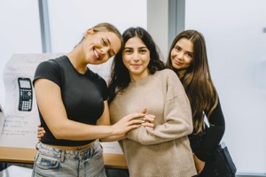 Three IAS Warsaw high school students standing arm in arm in a classroom, in front of a hand-drawn poster