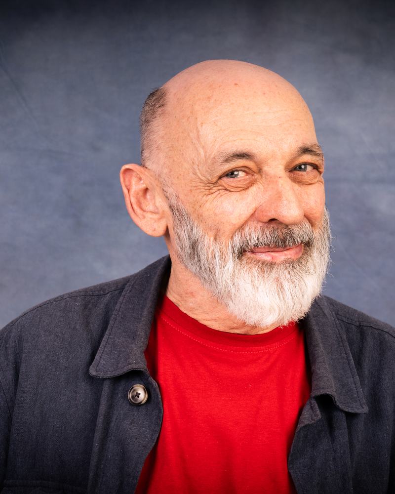 A smiling teacher at IAS Warsaw with a grey beard, in a red T-shirt and a dark jacket, studio portrait