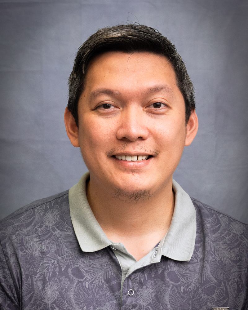 A smiling teacher at IAS Warsaw in a grey polo shirt, studio portrait