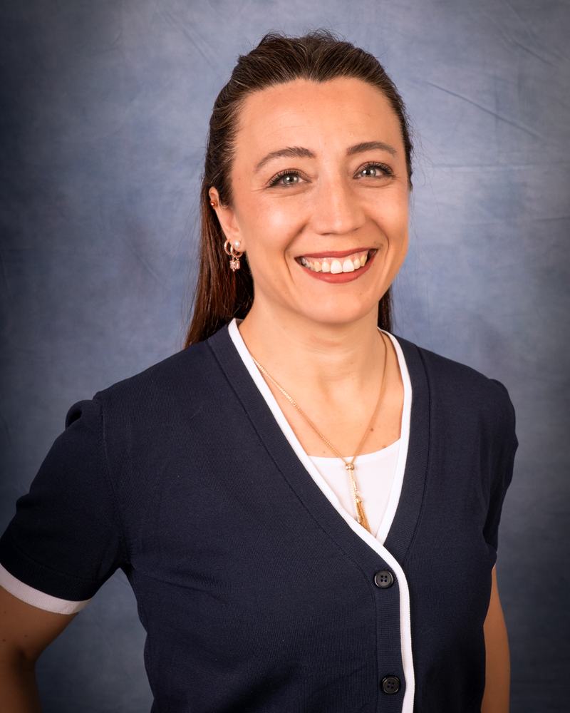 A smiling teacher at IAS Warsaw in a navy cardigan, studio portrait