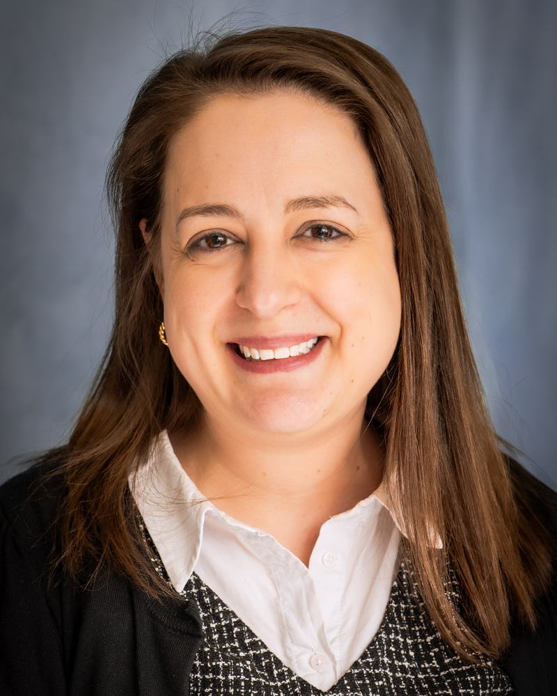 A smiling teacher at IAS Warsaw in a white collar and dark cardigan, studio portrait