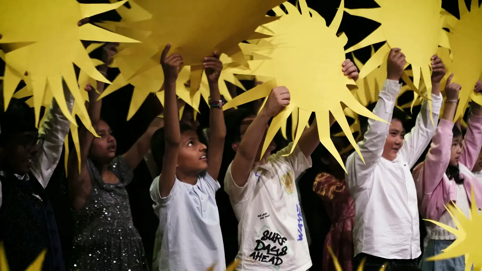 IAS pupils holding paper suns on stage