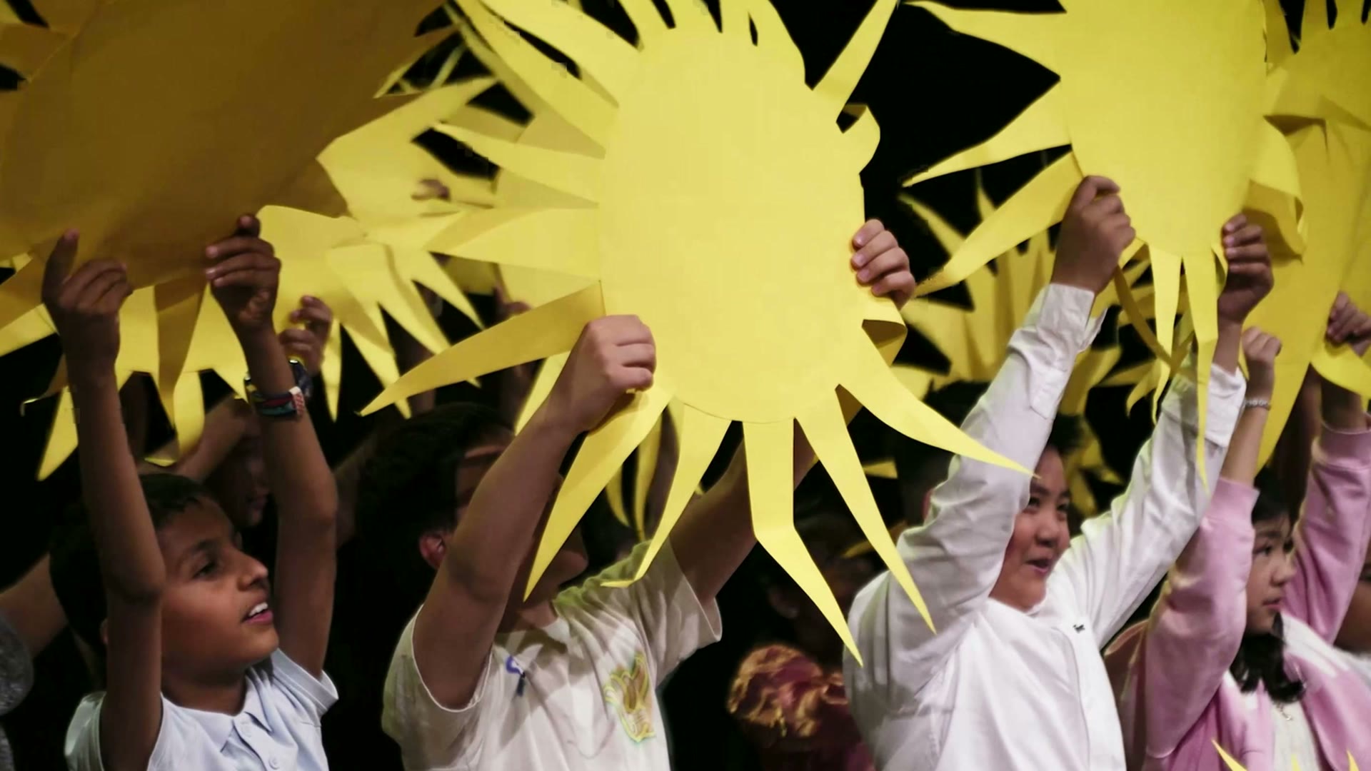 IAS pupils holding paper suns on stage