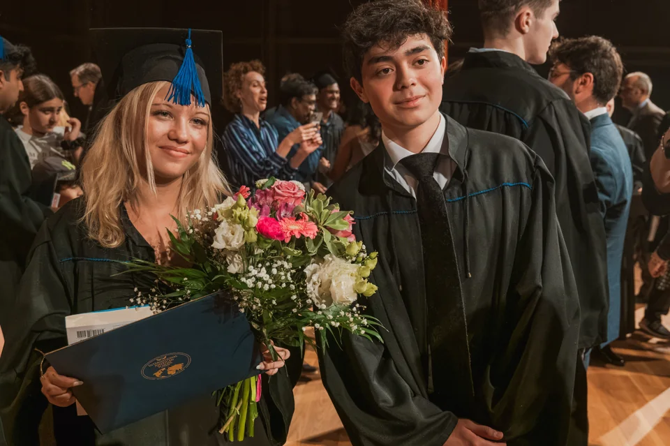 Two IAS graduates with diplomas and flowers